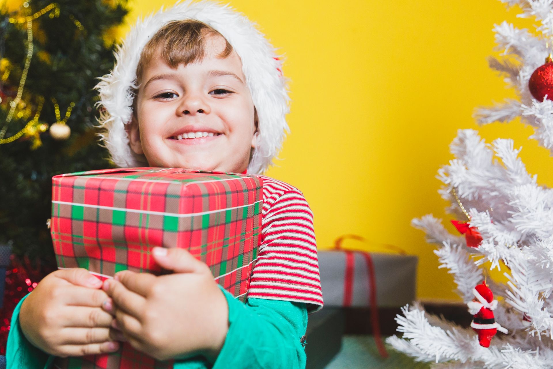 A young boy holding customized gift celebrating Christmas day near a Christmas tree